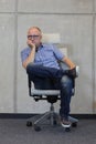 Middle age balding man with eyeglasses bad sitting position on chair in office Royalty Free Stock Photo
