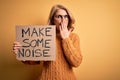 Middle age beautiful blonde activist woman holding banner with make some noise message cover mouth with hand shocked with shame
