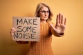 Middle age beautiful blonde activist woman holding banner with make some noise message with open hand doing stop sign with serious