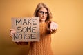 Middle age beautiful blonde activist woman holding banner with make some noise message pointing with finger to the camera and to Royalty Free Stock Photo