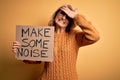 Middle age beautiful blonde activist woman holding banner with make some noise message stressed with hand on head, shocked with