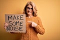 Middle age beautiful blonde activist woman holding banner with make some noise message very happy pointing with hand and finger