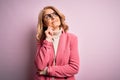 Middle age beautiful blonde business woman wearing elegant pink jacket and glasses with hand on chin thinking about question, Royalty Free Stock Photo