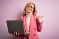 Middle age beautiful blonde business woman working using laptop over pink background pointing and showing with thumb up to the Royalty Free Stock Photo