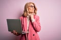 Middle age beautiful blonde business woman working using laptop over pink background serious face thinking about question, very Royalty Free Stock Photo