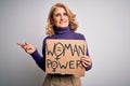 Middle age beautiful blonde woman asking for women rights holding banner very happy pointing with hand and finger to the side