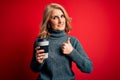 Middle age beautiful blonde woman drinking takeaway cup of coffee over red background happy with big smile doing ok sign, thumb up Royalty Free Stock Photo