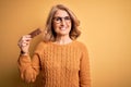 Middle age beautiful blonde woman eating energetic protein bar over yellow background with a happy face standing and smiling with Royalty Free Stock Photo