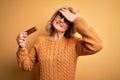 Middle age beautiful blonde woman eating energetic protein bar over yellow background stressed with hand on head, shocked with Royalty Free Stock Photo