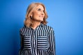 Middle age beautiful blonde woman wearing casual striped shirt standing over blue background looking away to side with smile on Royalty Free Stock Photo