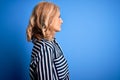 Middle age beautiful blonde woman wearing casual striped shirt standing over blue background looking to side, relax profile pose Royalty Free Stock Photo