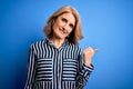 Middle age beautiful blonde woman wearing casual striped shirt standing over blue background smiling with happy face looking and Royalty Free Stock Photo