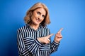 Middle age beautiful blonde woman wearing casual striped shirt standing over blue background smiling and looking at the camera Royalty Free Stock Photo