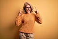 Middle age beautiful blonde woman wearing casual sweater and glasses over yellow background shouting with crazy expression doing Royalty Free Stock Photo