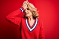 Middle age beautiful blonde woman wearing casual sweater over isolated red background surprised with hand on head for mistake, Royalty Free Stock Photo