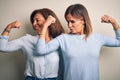 Middle age beautiful couple of sisters standing over isolated white background showing arms muscles smiling proud