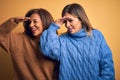 Middle age beautiful couple of sisters wearing casual sweater over isolated yellow background very happy and smiling looking far Royalty Free Stock Photo