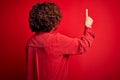 Middle age beautiful curly hair woman wearing casual shirt and glasses over red background Posing backwards pointing ahead with Royalty Free Stock Photo