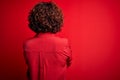 Middle age beautiful curly hair woman wearing casual shirt and glasses over red background standing backwards looking away with Royalty Free Stock Photo