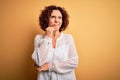 Middle age beautiful curly hair woman wearing casual summer dress over yellow background with hand on chin thinking about Royalty Free Stock Photo