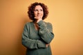 Middle age beautiful curly hair woman wearing casual sweater over isolated yellow background with hand on chin thinking about Royalty Free Stock Photo