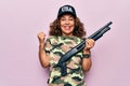 Middle age beautiful hunter woman wearing camouflage t-shirt and usa cap holding shotgun screaming proud, celebrating victory and Royalty Free Stock Photo