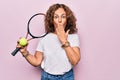 Middle age beautiful sportswoman playing tennis holding racket and ball over white background covering mouth with hand, shocked Royalty Free Stock Photo