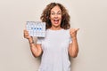 Middle age beautiful woman holding climatology calendar showing cloudy and rainy weather pointing thumb up to the side smiling