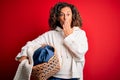 Middle age beautiful woman holding wicker basket with clothes over isolated red background cover mouth with hand shocked with Royalty Free Stock Photo