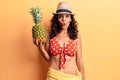 Middle age beautiful woman wearing bikini and summer hat holding pineappel scared and amazed with open mouth for surprise, Royalty Free Stock Photo