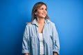 Middle age beautiful woman wearing casual shirt standing over isolated blue background looking away to side with smile on face, Royalty Free Stock Photo