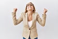 Middle age blonde business woman standing over isolated background celebrating surprised and amazed for success with arms raised Royalty Free Stock Photo