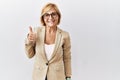 Middle age blonde business woman standing over isolated background doing happy thumbs up gesture with hand Royalty Free Stock Photo
