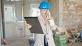 Middle age blonde woman architect talking on smartphone reading document at construction site Royalty Free Stock Photo