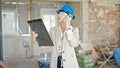 Middle age blonde woman architect talking on smartphone reading document at construction site Royalty Free Stock Photo