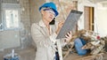 Middle age blonde woman architect talking on smartphone writing on document at construction site Royalty Free Stock Photo