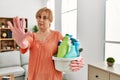 Middle age blonde woman holding cleaning products cleaning at home with open hand doing stop sign with serious and confident Royalty Free Stock Photo