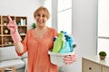 Middle age blonde woman holding cleaning products cleaning at home smiling happy pointing with hand and finger to the side Royalty Free Stock Photo