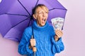 Middle age blonde woman holding umbrella and russian ruble banknotes angry and mad screaming frustrated and furious, shouting with Royalty Free Stock Photo