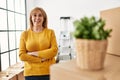 Middle age blonde woman standing with arms crossed gesture at new home Royalty Free Stock Photo
