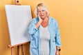 Middle age blonde woman standing by painter easel stand thinking looking tired and bored with depression problems with crossed