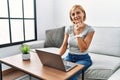 Middle age blonde woman using laptop at home looking confident at the camera smiling with crossed arms and hand raised on chin Royalty Free Stock Photo