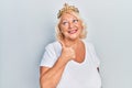 Middle age blonde woman wearing queen crown smiling with happy face looking and pointing to the side with thumb up Royalty Free Stock Photo