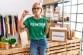 Middle age blonde woman wearing volunteer t shirt holding charity money with angry face, negative sign showing dislike with thumbs