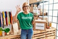 Middle age blonde woman wearing volunteer t shirt holding charity money doing ok sign with fingers, smiling friendly gesturing