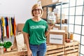 Middle age blonde woman wearing volunteer t shirt holding charity money looking positive and happy standing and smiling with a