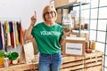 Middle age blonde woman wearing volunteer t shirt holding charity money surprised with an idea or question pointing finger with