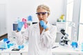 Middle age blonde woman working at laboratory looking for breast cancer cure serious face thinking about question with hand on
