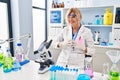 Middle age blonde woman working at scientist laboratory hands together and fingers crossed smiling relaxed and cheerful