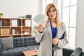 Middle age blonde woman working at therapy consultation office holding money clueless and confused expression Royalty Free Stock Photo